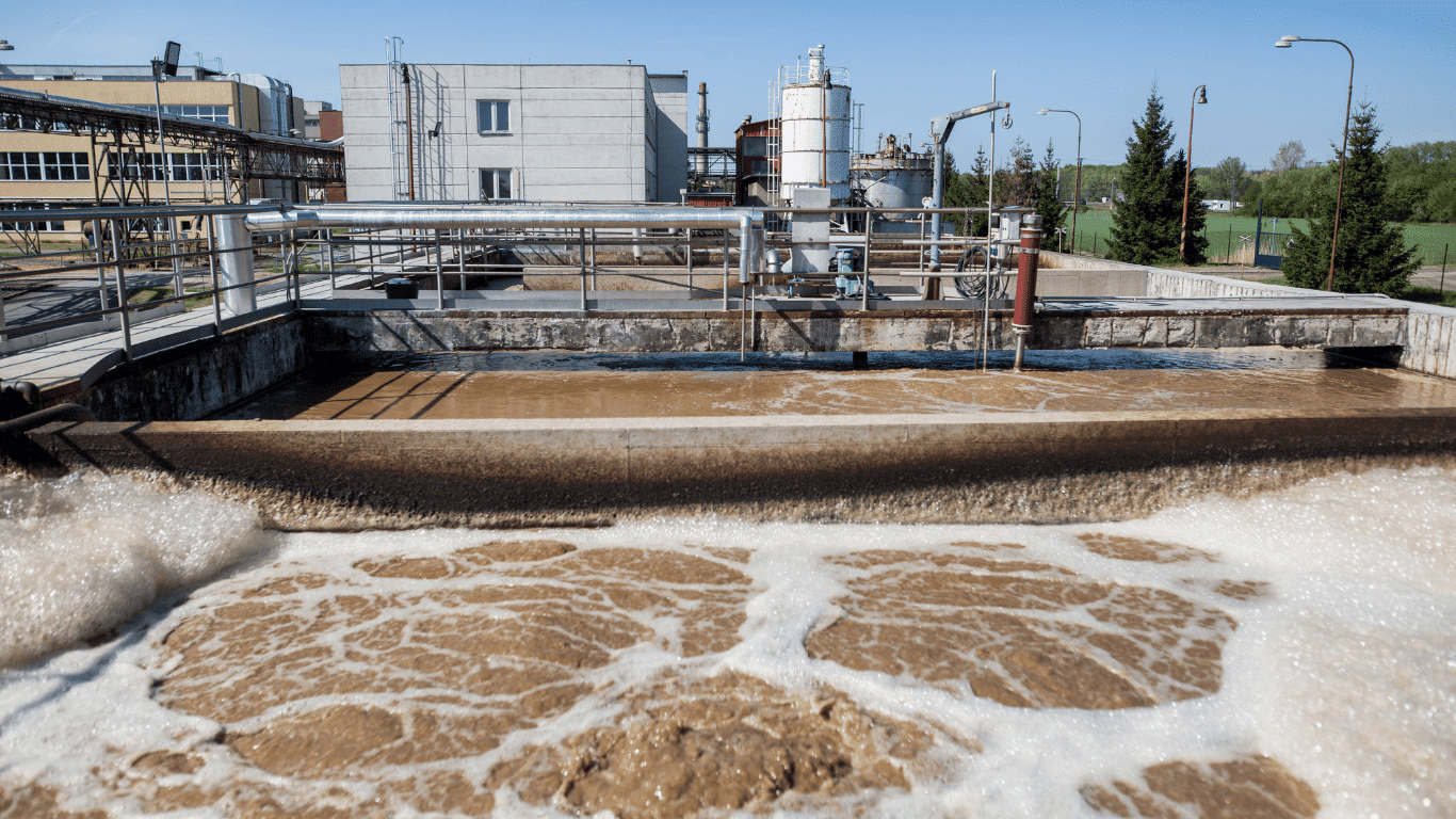 An outdoor view of a wastewater treatment plant showing aeration tanks where wastewater and sewage from various sources are processed to explain what is effluent. The image illustrates how a sewage treatment plant and municipal sewage treatment plants generate wastewater and move it through the initial stage of primary treatment in a treatment plant to remove pollutants, contaminants, and suspended solids from trade effluent, stormwater, and industrial outfall entering through drainage pipes. The flowing brown water represents untreated wastes before they are treated to create cleaner effluent that can be safely discharged into water bodies, surface water, or a septic tank, depending on other conditions and safety requirements. This scene supports understanding effluent as the liquid waste that wastes digest during wastewater treatment, showing how both two terms—wastewater and effluent—relate. The content aligns with coverage commonly found in Endeavor Business Media resources about pollutants, treatment processes, and environmental impacts.